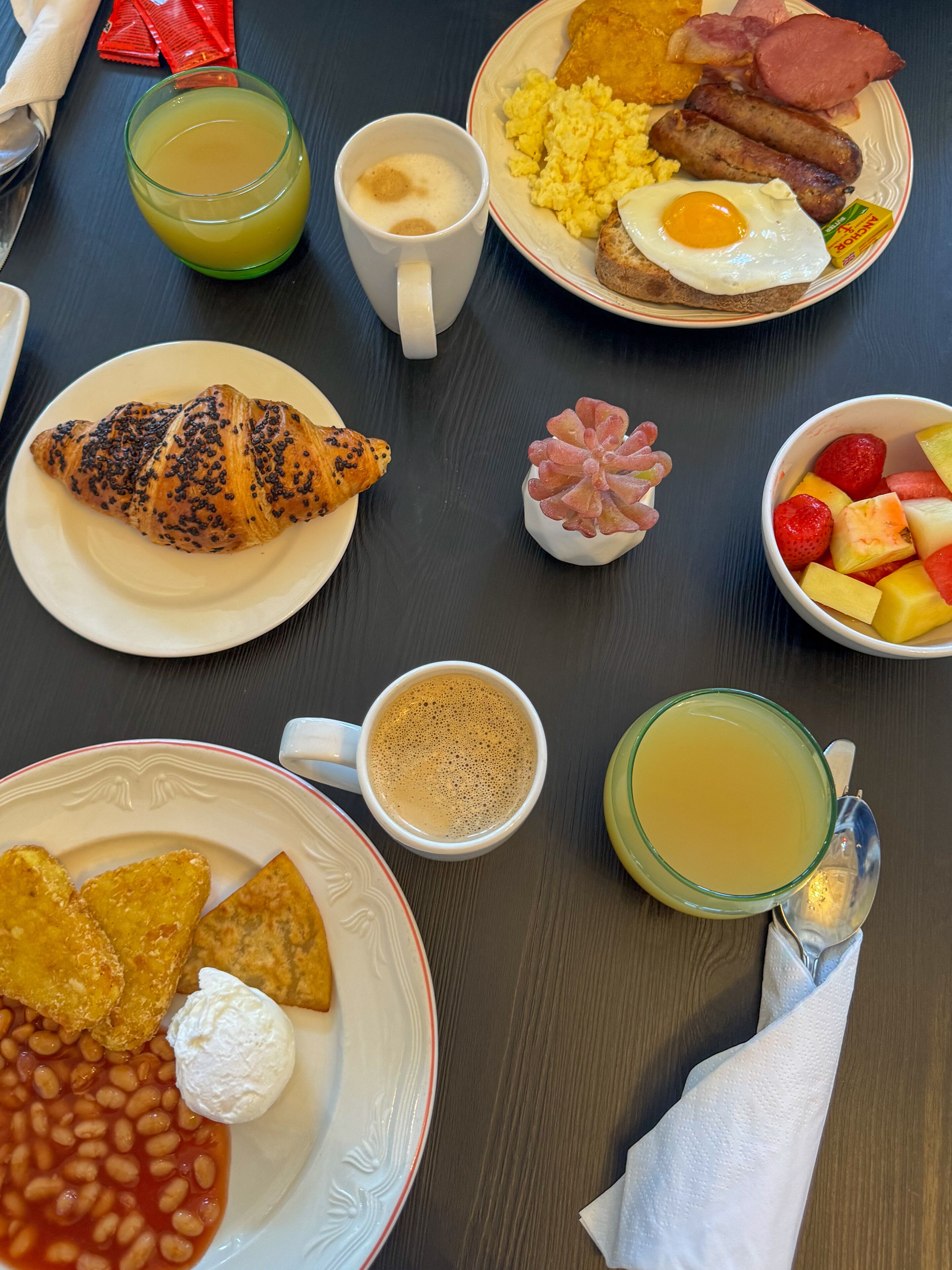 Una mesa de desayuno con diferentes platos, como huevos, salchichas, tostadas y fruta.