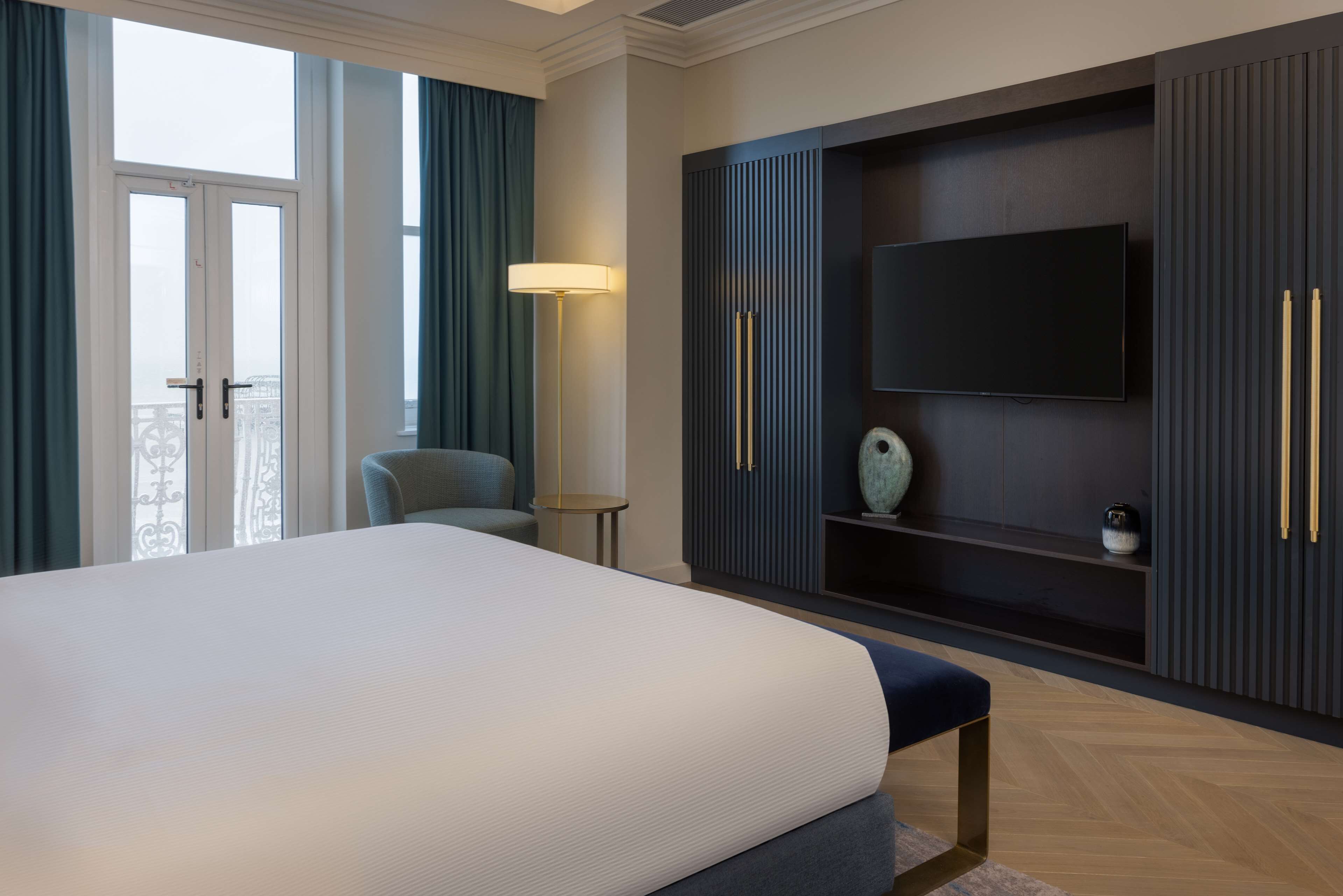 Ein modernes Hotelzimmer mit einem großen Bett, einem an einer dunklen Wand montierten Fernseher und einem Balkon mit Vorhängen.