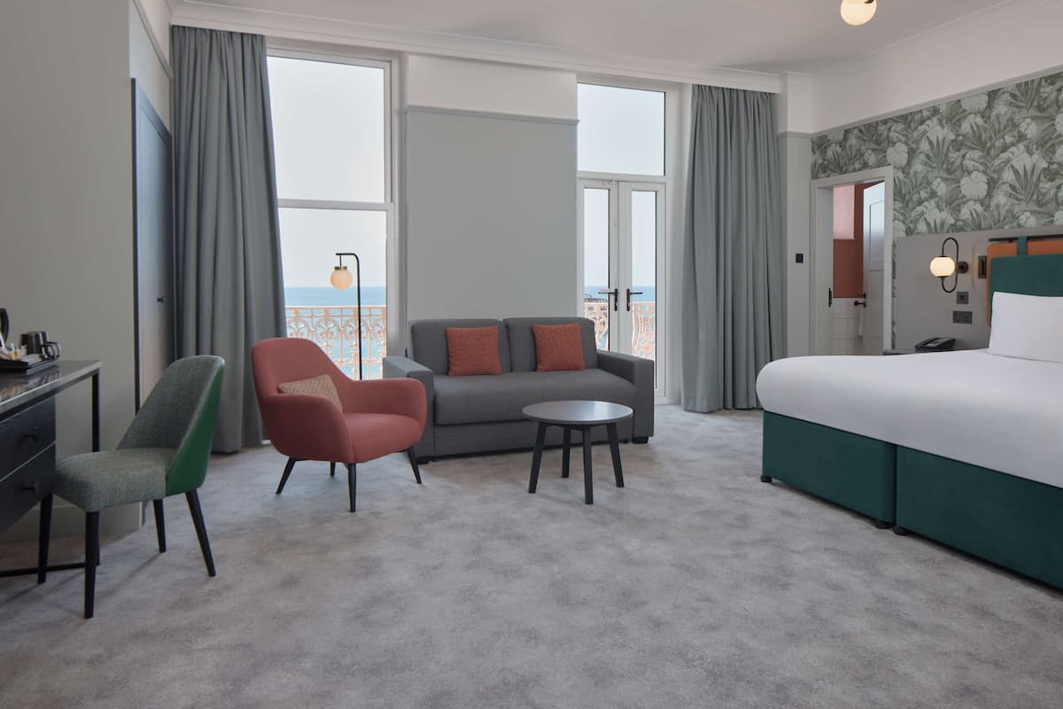 A hotel room with a bed, a sofa, two chairs, a small table, and a desk.