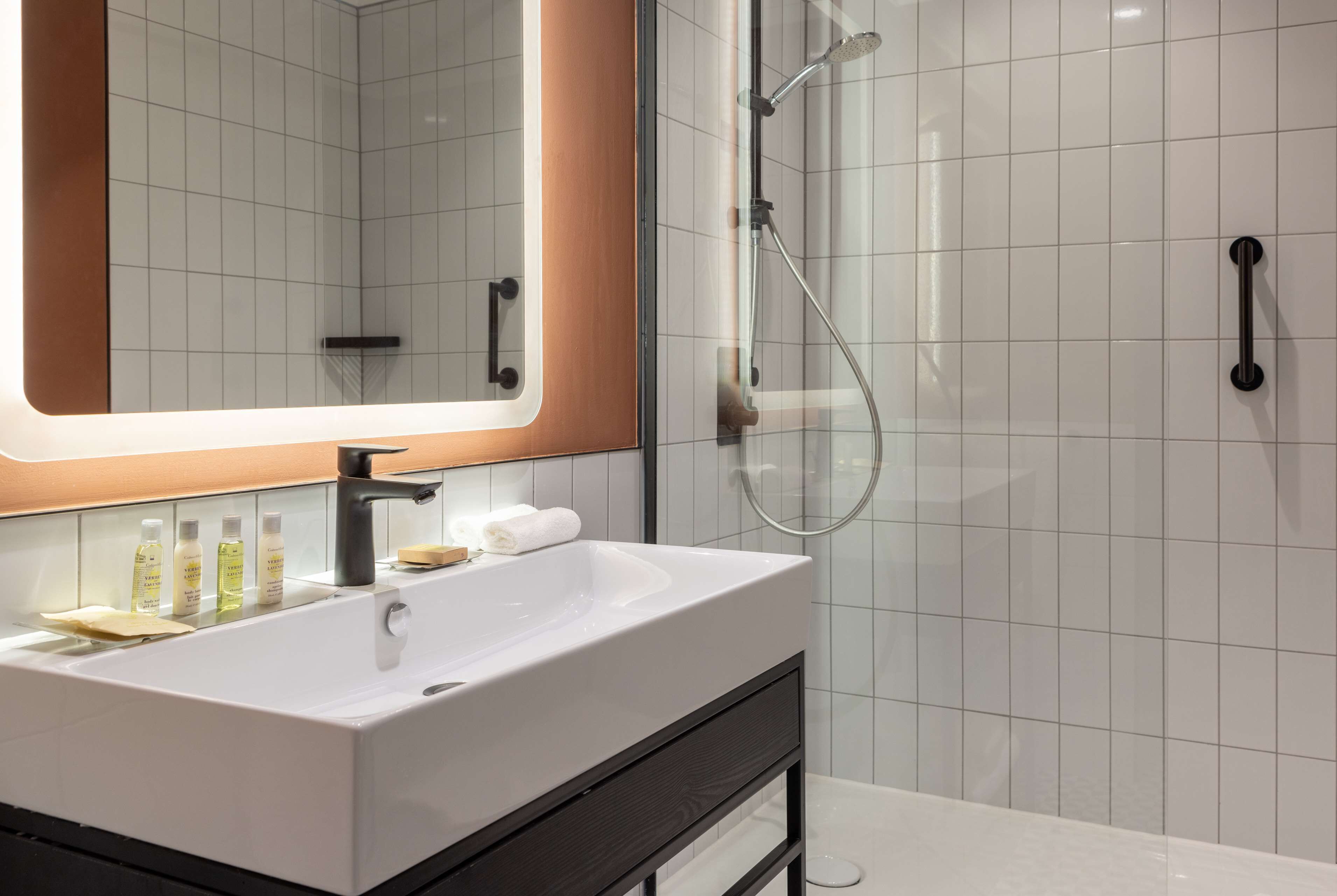 Un baño moderno con un espejo grande, un lavamanos blanco y una ducha con mampara de vidrio.