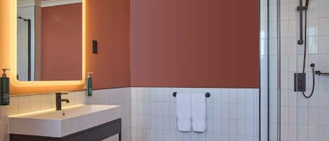 Une salle de bain avec un lavabo blanc, un miroir, un porte-serviettes et un espace douche.