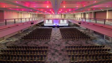 Un salón de conferencias amplio con filas de sillas, un escenario y un balcón.
