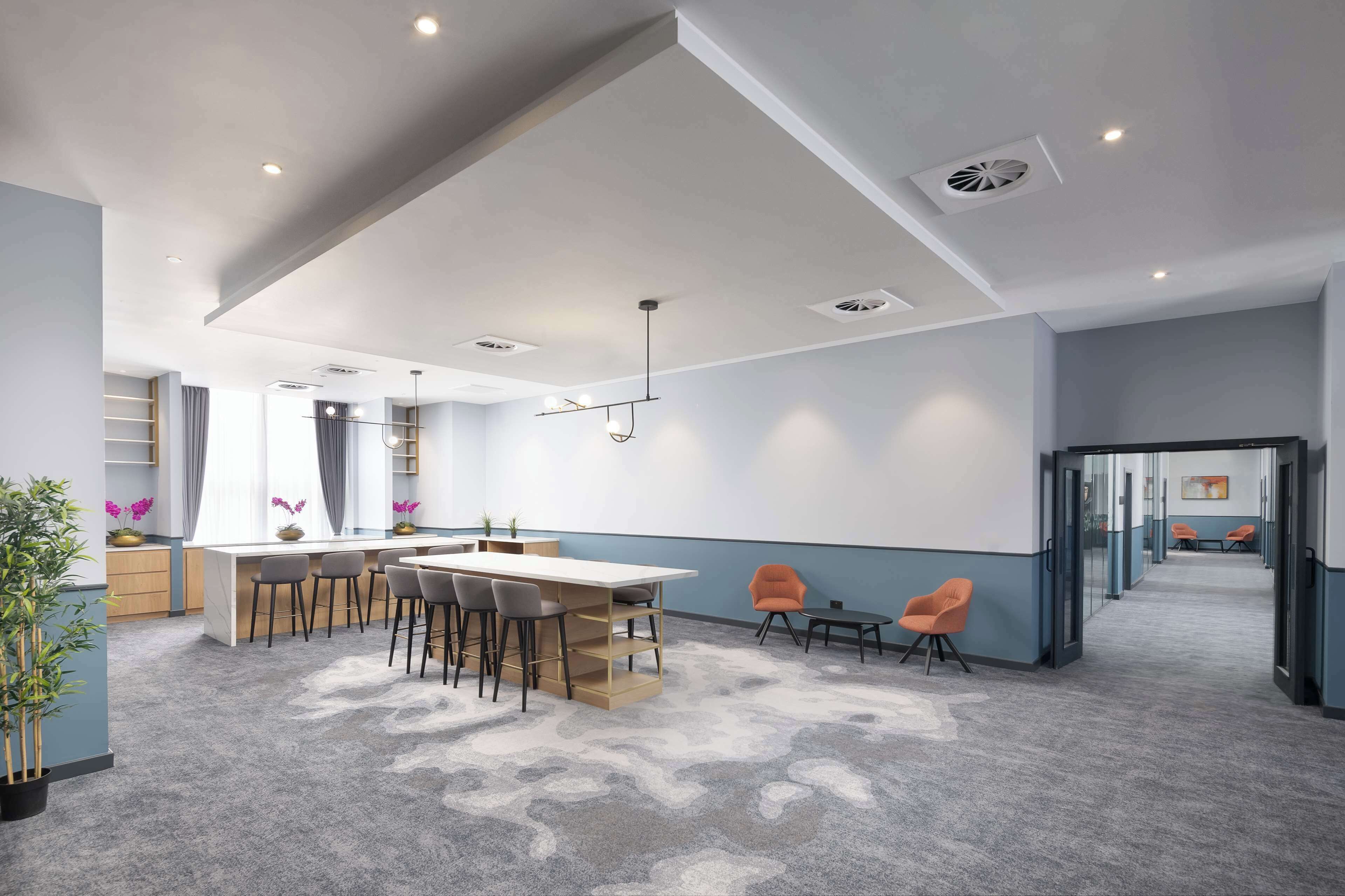 A modern office space with a central table, chairs, and a long corridor with seating areas.