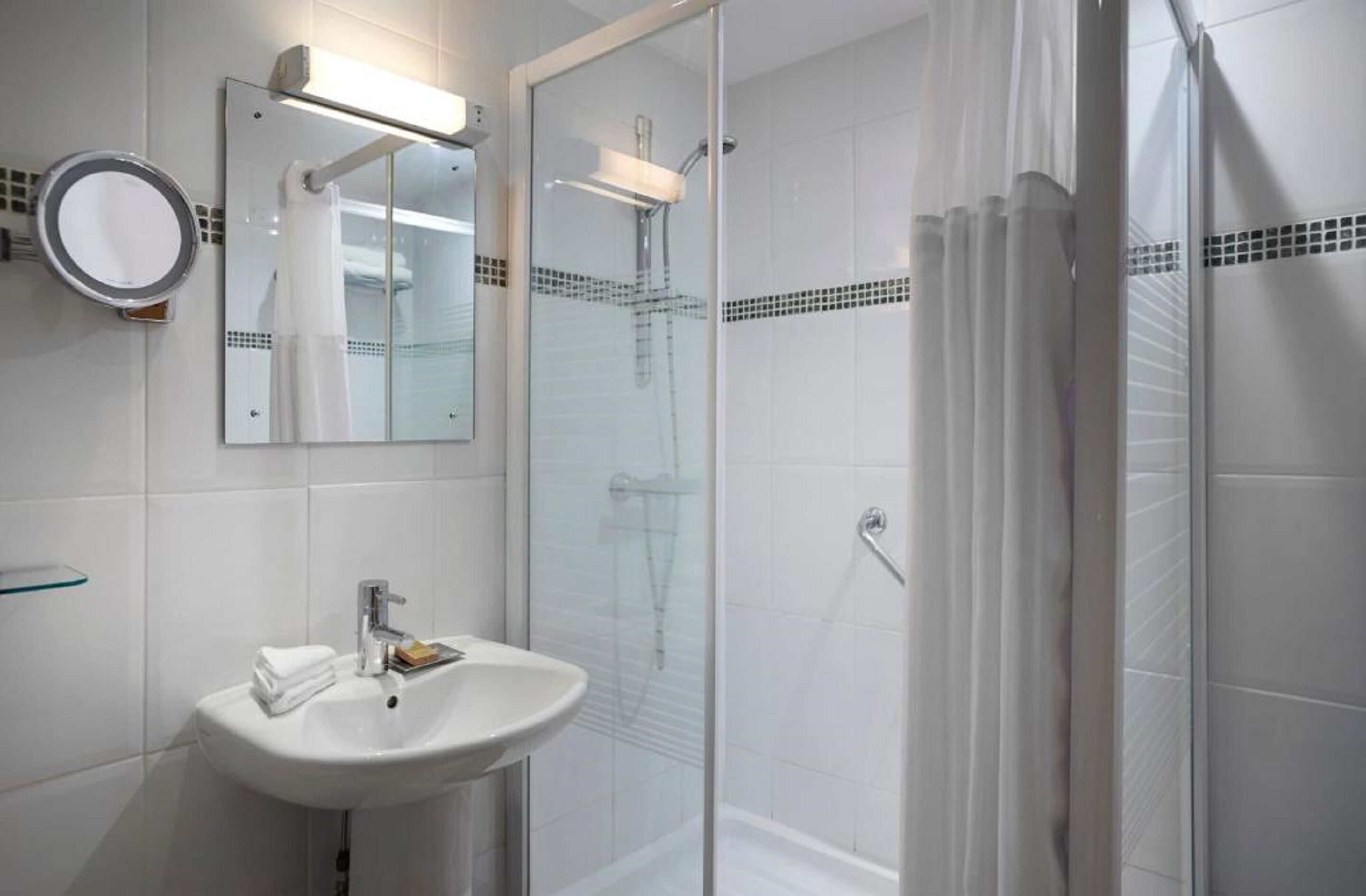 Un baño con ducha de vidrio, un lavabo con espejo y un estante de vidrio.