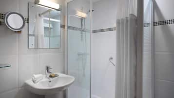 Un baño con ducha de vidrio, un lavabo con espejo y un estante de vidrio.
