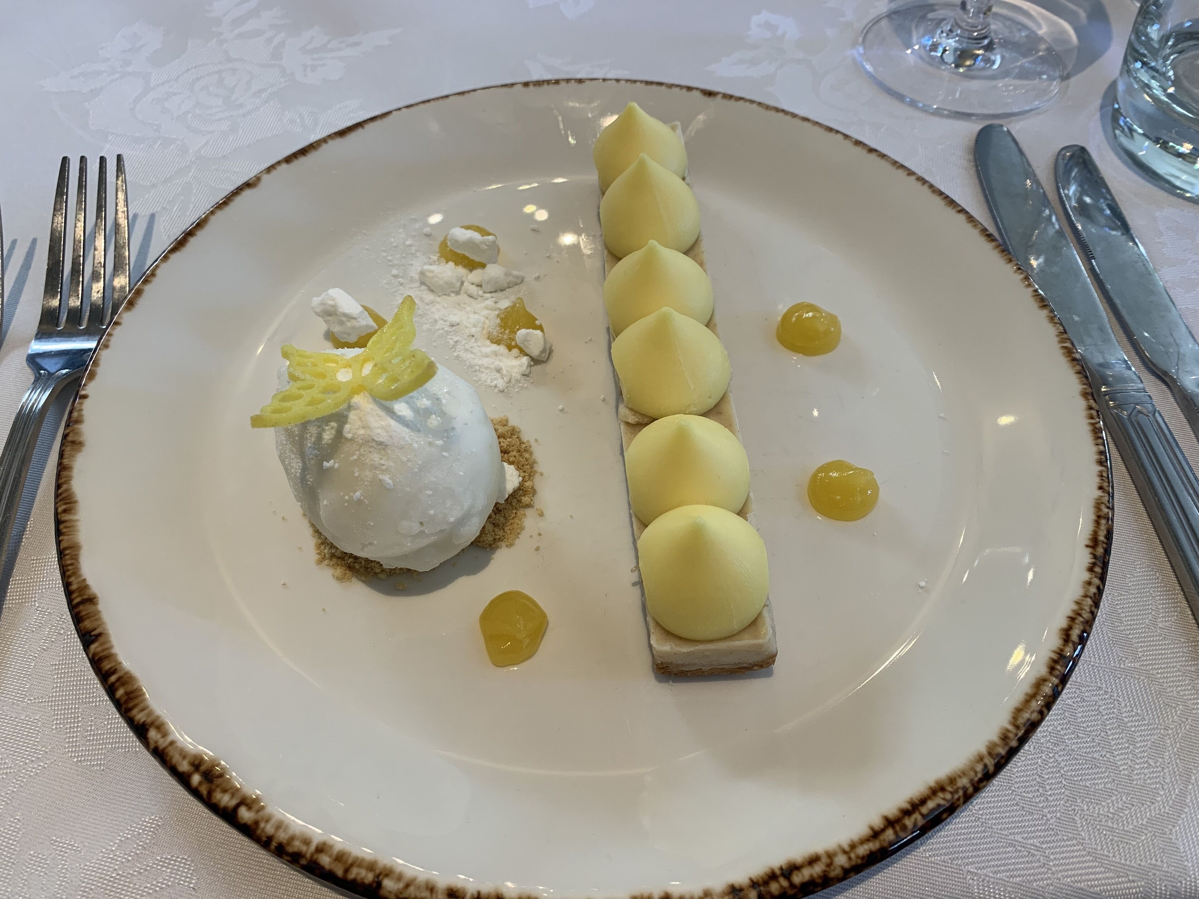 Ein Dessertteller mit einer Kugel Eis, einem rechteckigen Kuchenstück und kleinen gelben Kugeln.