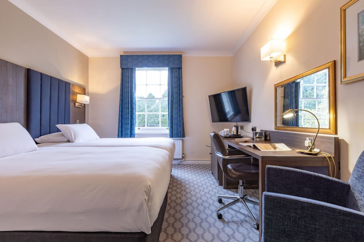 A hotel room with a large bed, a desk with a chair, a television, and a window with curtains.