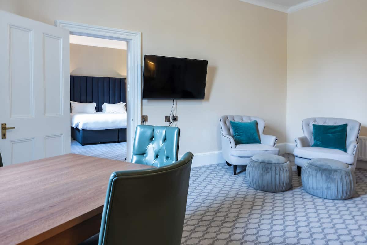A hotel room with a bed, a TV, a dining table, and two armchairs.
