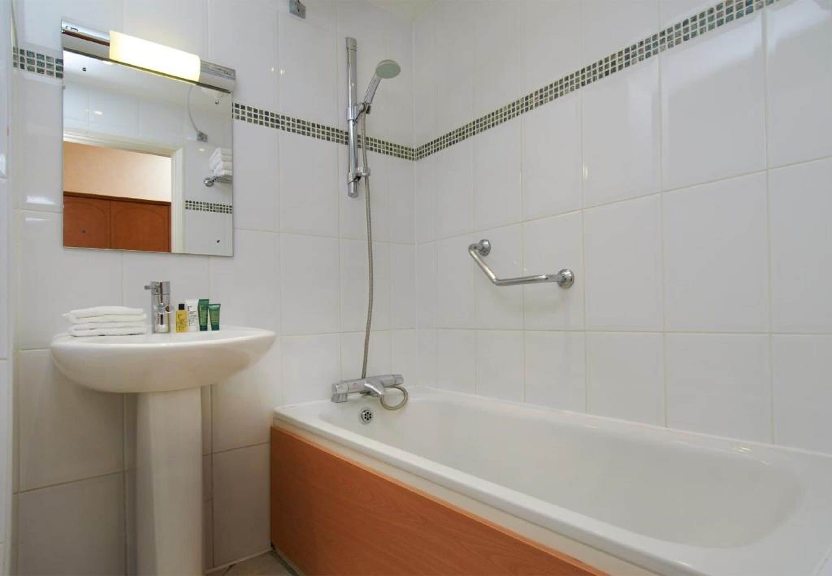 Un baño con lavamanos blanco, espejo y bañera.