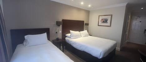 Habitación de hotel con dos camas, una mesita de noche, una lámpara de pared y una puerta que da al baño.