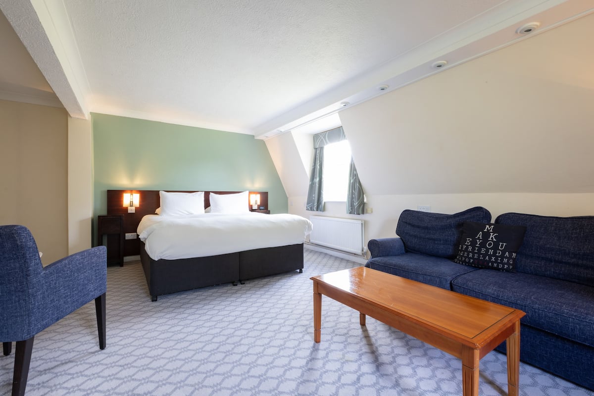 A hotel room with a bed, a sofa, a coffee table, and a chair.