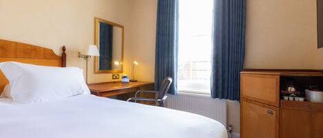 Une chambre d’hôtel avec un grand lit, un bureau avec une lampe, une chaise, une armoire et une fenêtre avec des rideaux.