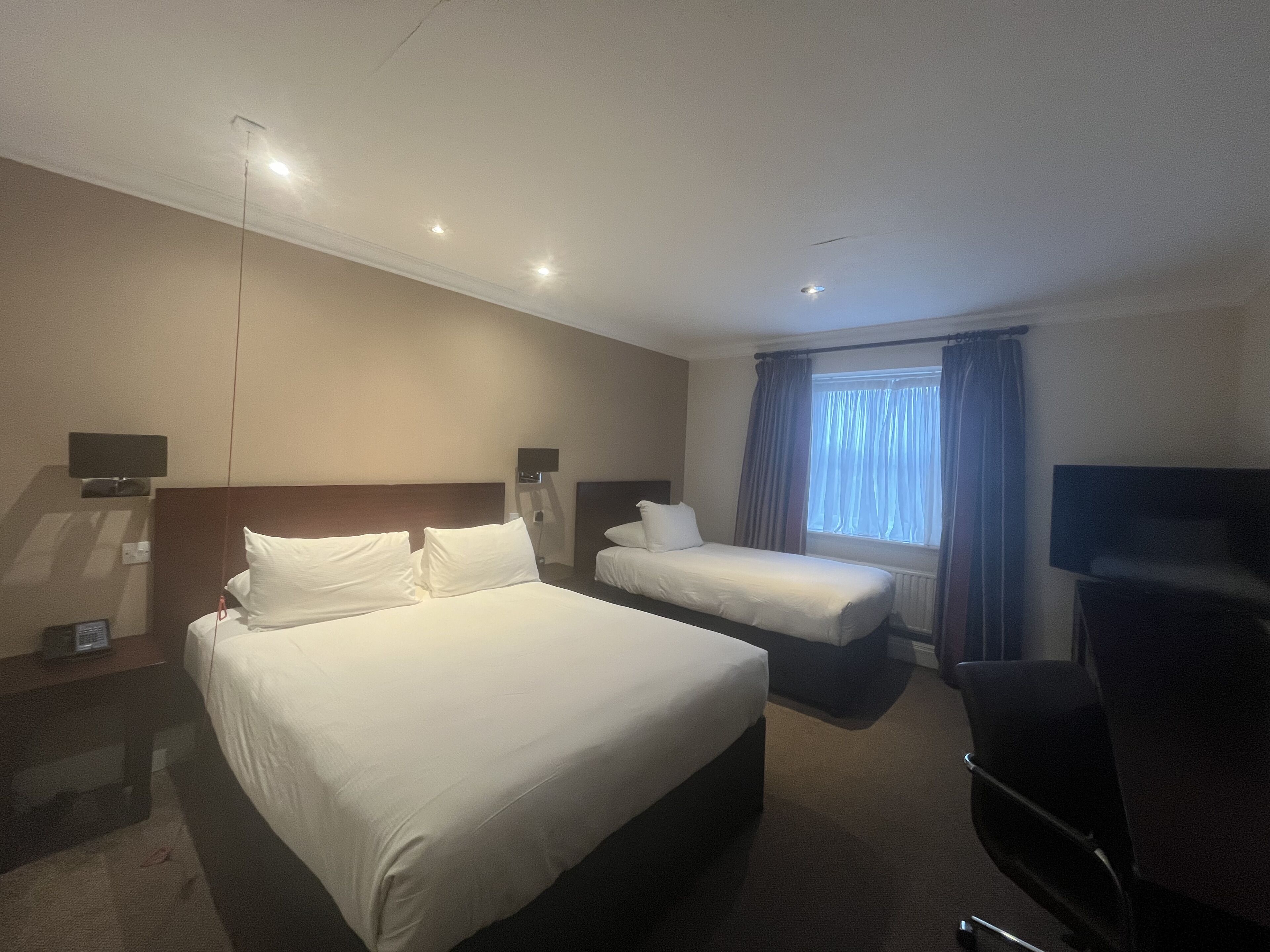 A hotel room with two single beds, a flat-screen TV, and a window with curtains.