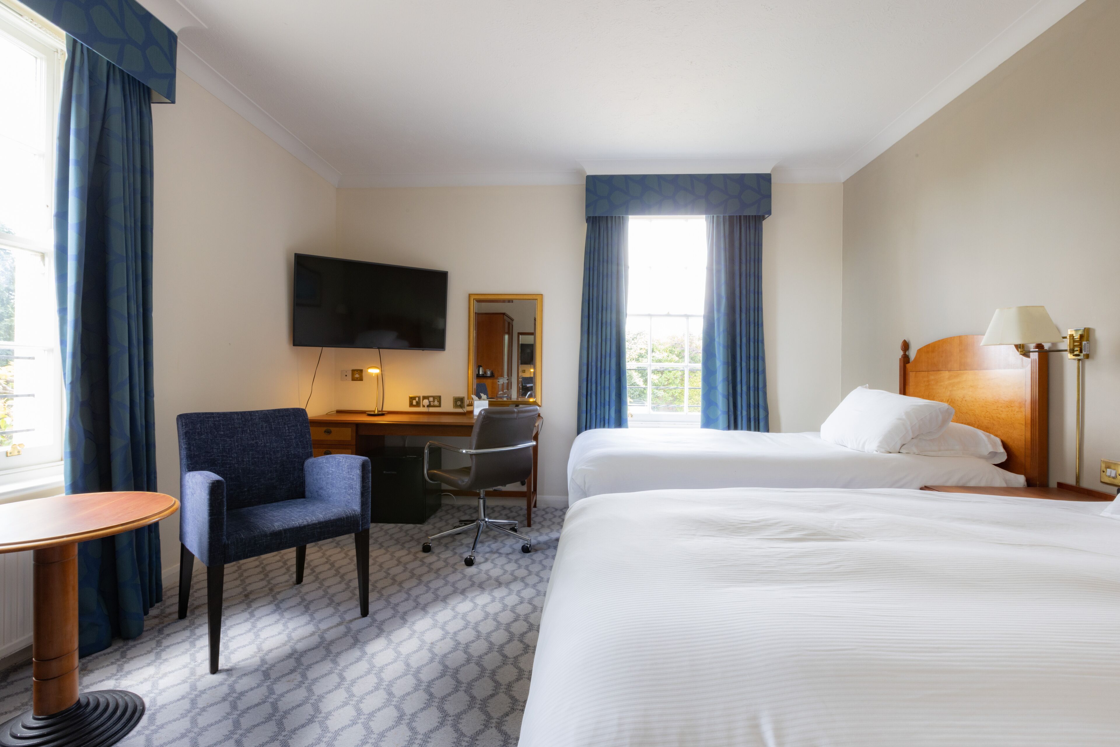A hotel room with a large bed, a desk with a chair, a TV, and a window with curtains.