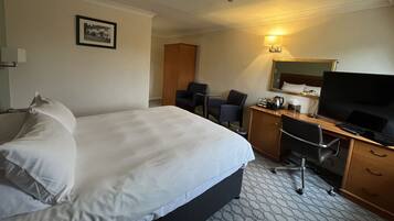 A hotel room with a bed, desk, chair, television, and a framed picture on the wall.