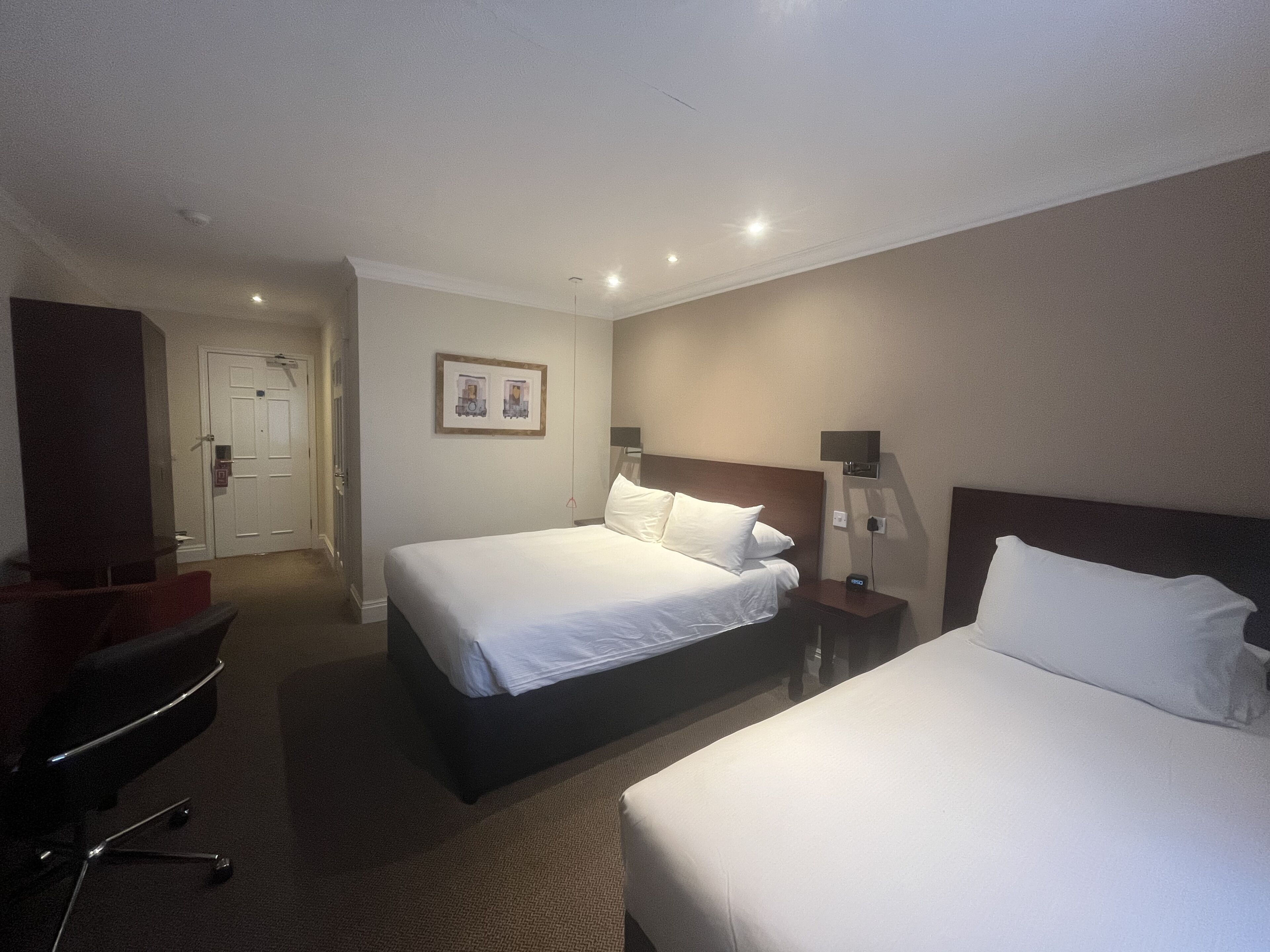 A hotel room with two beds, a desk, a chair, a TV, and a framed picture on the wall.
