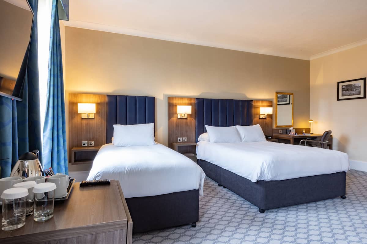 A hotel room with two beds, bedside lamps, a desk, and a chair.