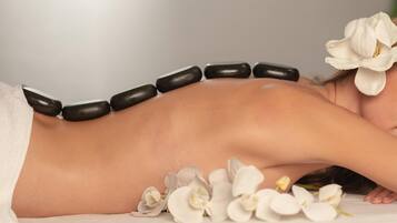 Une personne allongée sur une table de massage, entourée de pierres et de fleurs blanches.