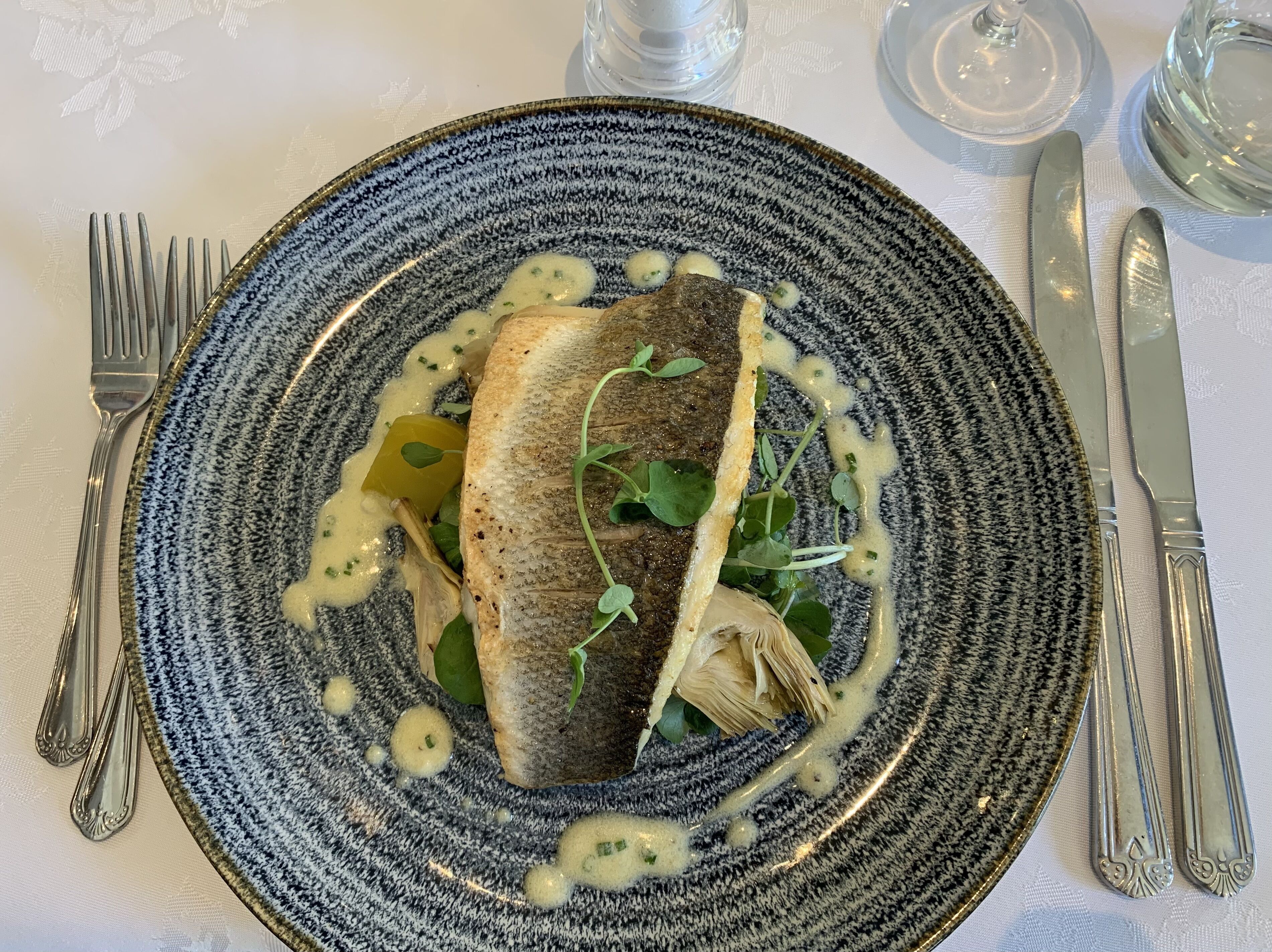 Um prato com peixe, vegetais e molho sobre um prato texturizado.