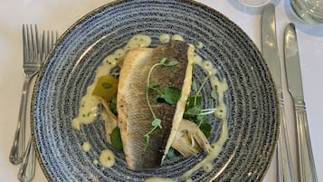 Um prato com peixe, vegetais e molho sobre um prato texturizado.