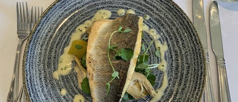 A plate with a fish, greens, and sauce on a textured plate.