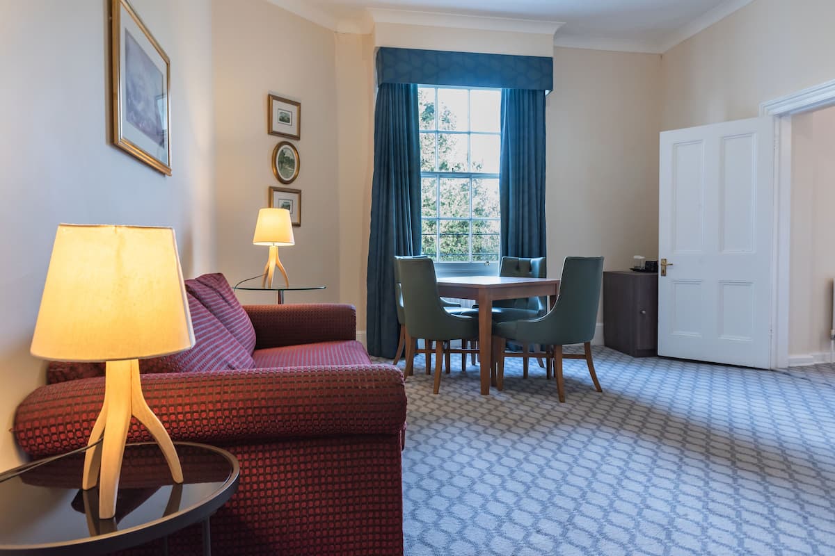 A room with a sofa, a table with chairs, a lamp, and a door.