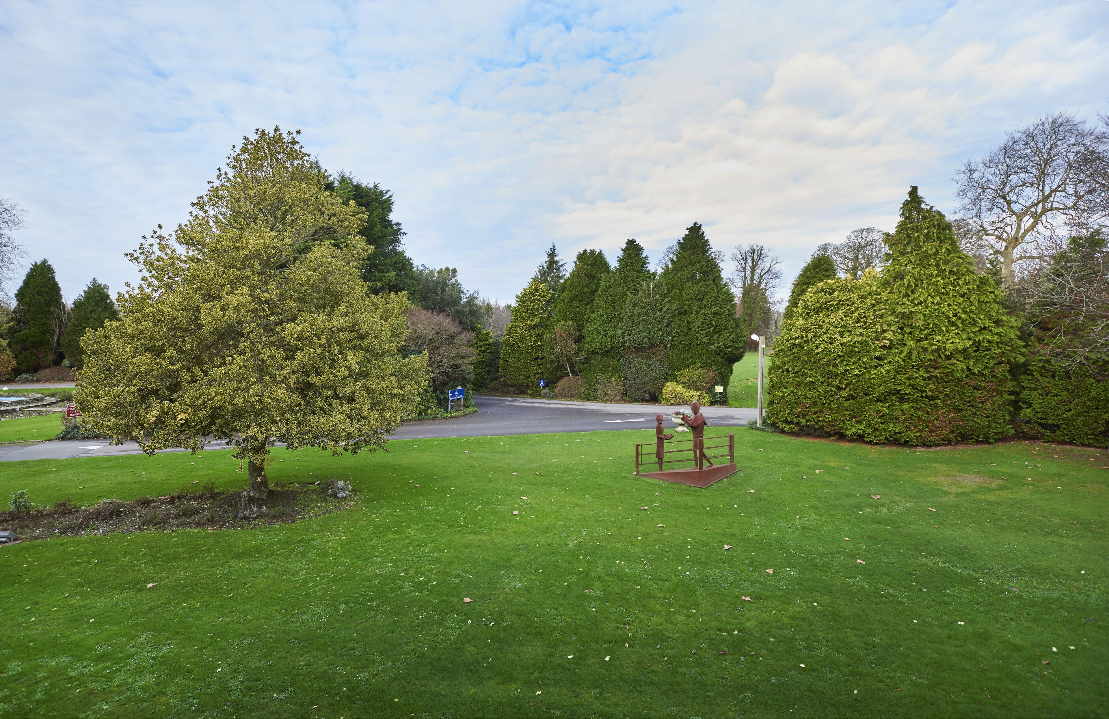 A park with a statue, a well-maintained lawn, and a road in the background.