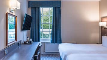 Habitación de hotel con cama, escritorio con silla, televisor y ventana con cortinas.