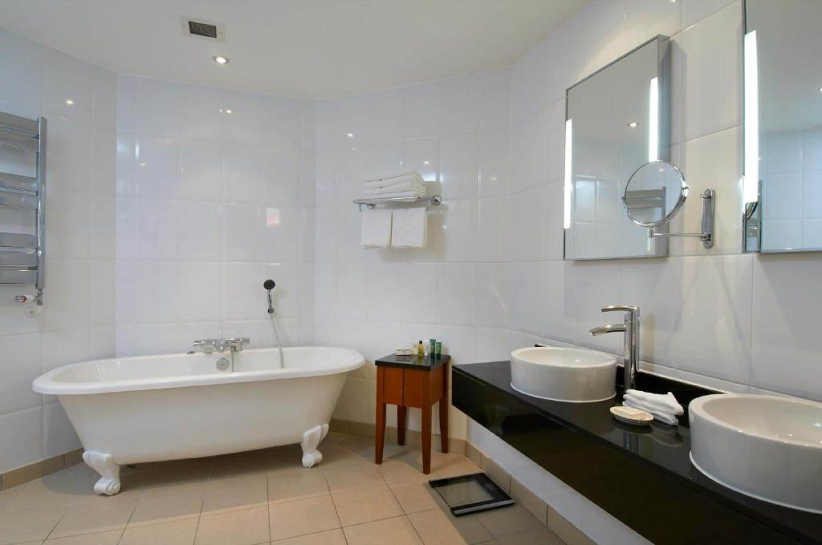 Een moderne badkamer met een vrijstaand bad, twee wastafels en een grote spiegel.