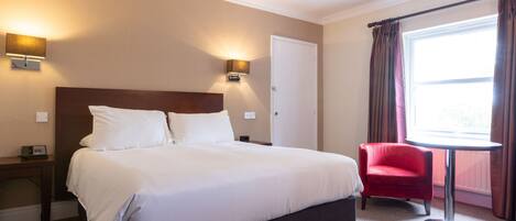 A hotel room with a large bed, two bedside lamps, a red chair, and a window with curtains.