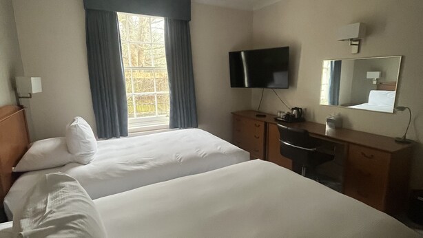 A hotel room with two beds, a desk, a chair, a television, and a window with curtains. - Avisford Park Hotel (Arundel)