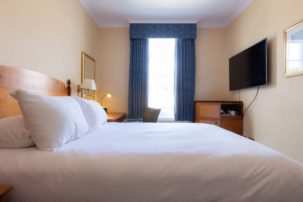 A hotel room with a large bed, a flat-screen TV, a desk, and a chair.