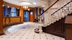 A grand lobby with a marble floor, a reception desk, a staircase with ornate railings, and a chandelier. - Avisford Park Hotel (Arundel)