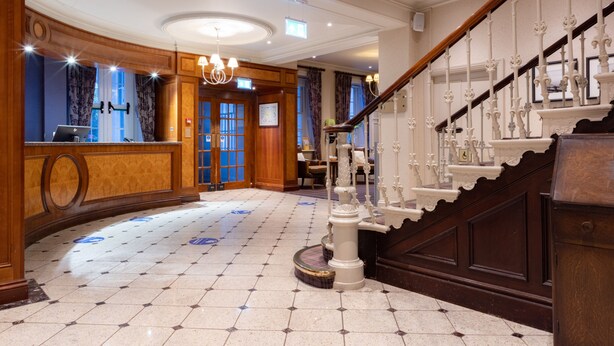 A grand lobby with a marble floor, a reception desk, a staircase with ornate railings, and a chandelier. - Avisford Park Hotel (Arundel)