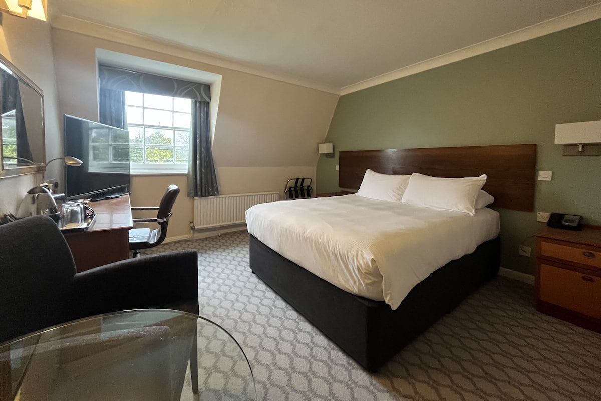 A hotel room with a large bed, a desk with a chair, a television, and a window with curtains.