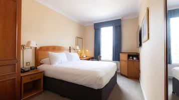 A hotel room with a large bed, bedside tables, a desk, a chair, and a television.