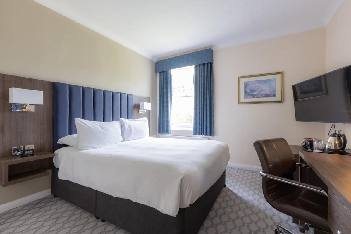 A hotel room with a large bed, a desk with a chair, a television, and a window with curtains.