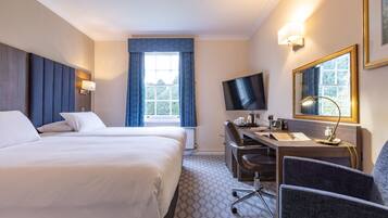 Een hotelkamer met een groot bed, een bureau met stoel, een televisie en een raam met gordijnen.