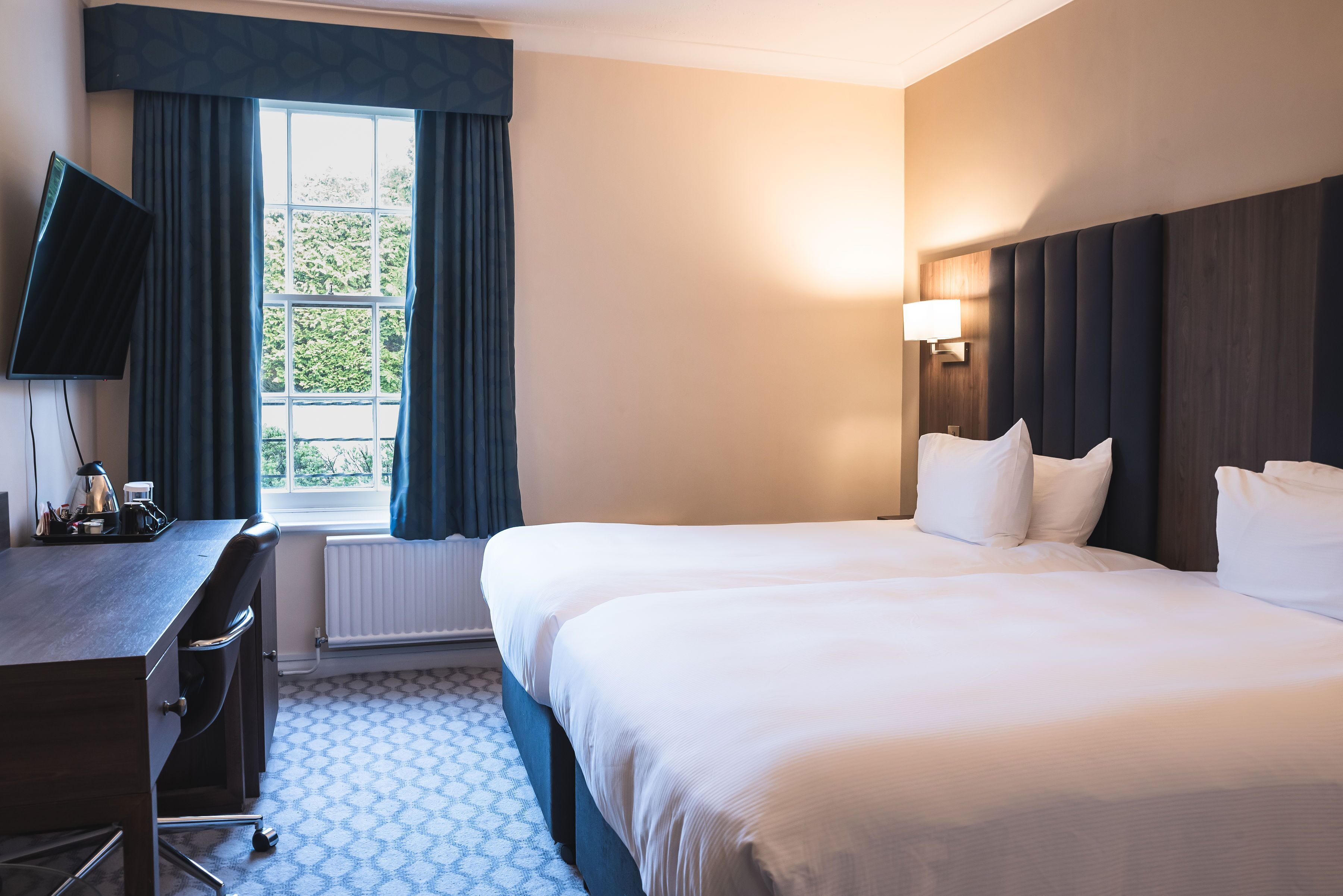 Habitación de hotel con una cama grande, un escritorio con silla, televisor de pantalla plana y ventana con cortinas.