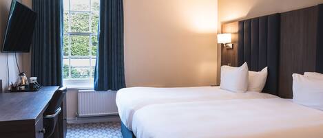 Habitación de hotel con una cama grande, un escritorio con silla, televisor de pantalla plana y ventana con cortinas.