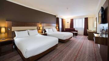A hotel room with two beds, a desk, a chair, and a TV.