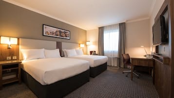 Habitación de hotel con dos camas, un escritorio, una silla, un televisor y un cuadro en la pared.