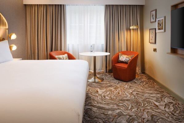 A hotel room with a large bed, two armchairs, a small round table, and a TV on the wall. - DoubleTree by Hilton Bristol North (Bristol)