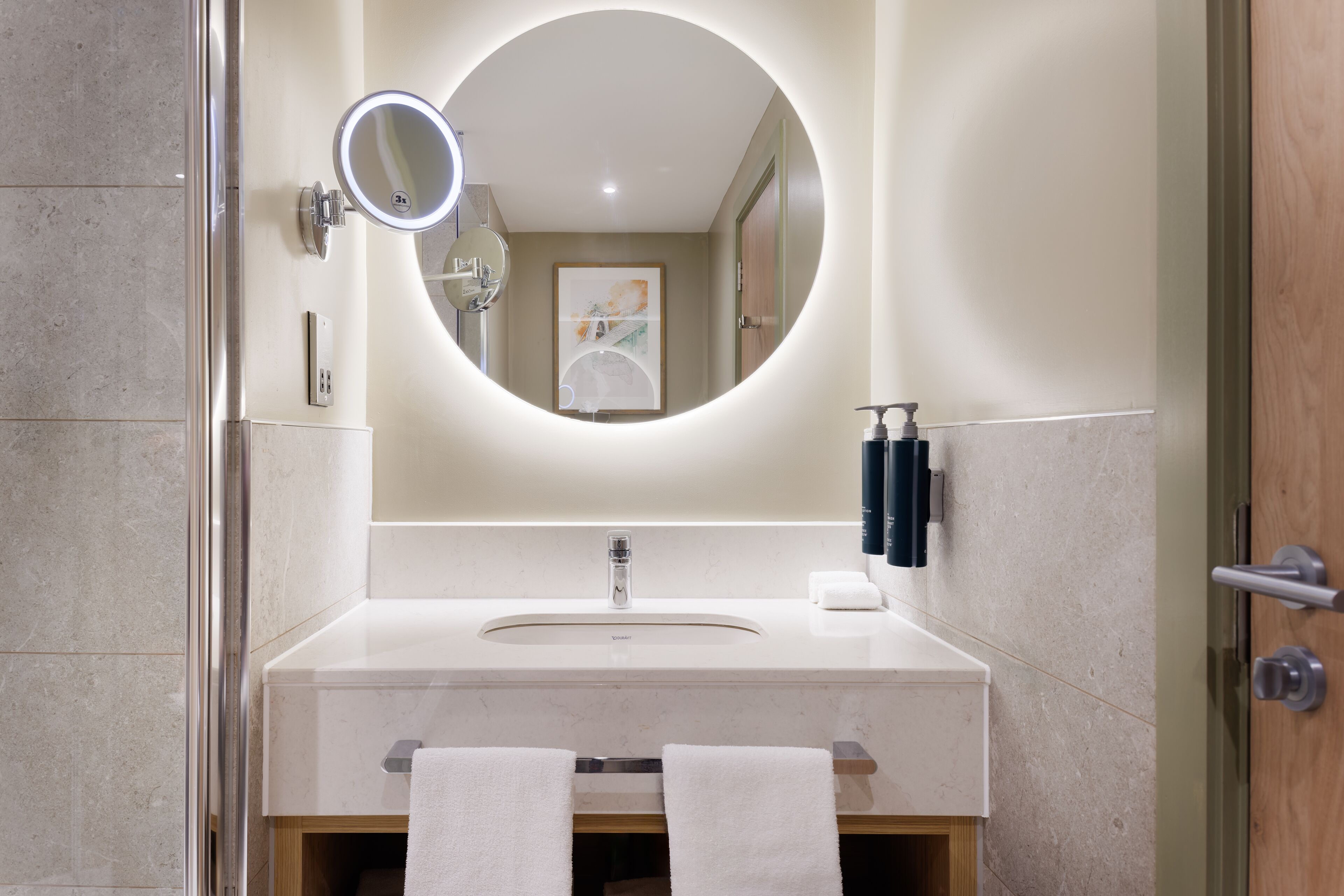A modern bathroom with a round mirror, a sink, and two towels hanging on a rack.