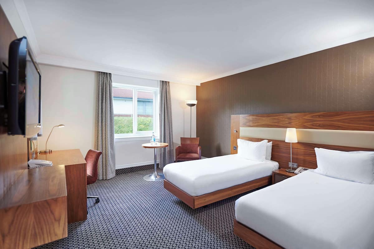A hotel room with two beds, a desk, a chair, a lamp, and a TV.