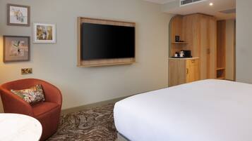 A hotel room with a bed, a TV mounted on the wall, a wooden wardrobe, a red armchair, and a patterned carpet.