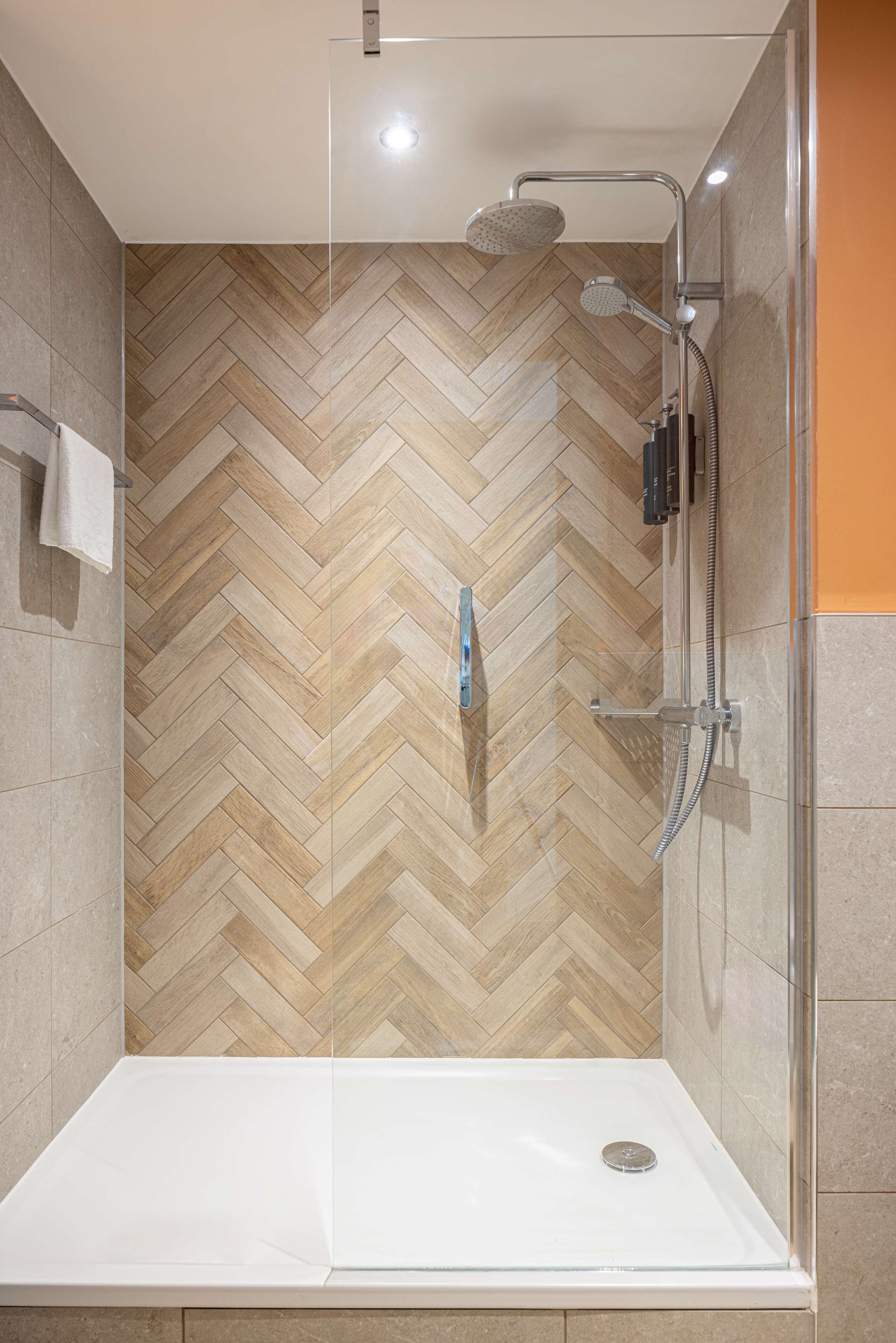 Un espace douche moderne avec un sol en bois disposé en chevrons, une paroi de douche en verre et une baignoire blanche.