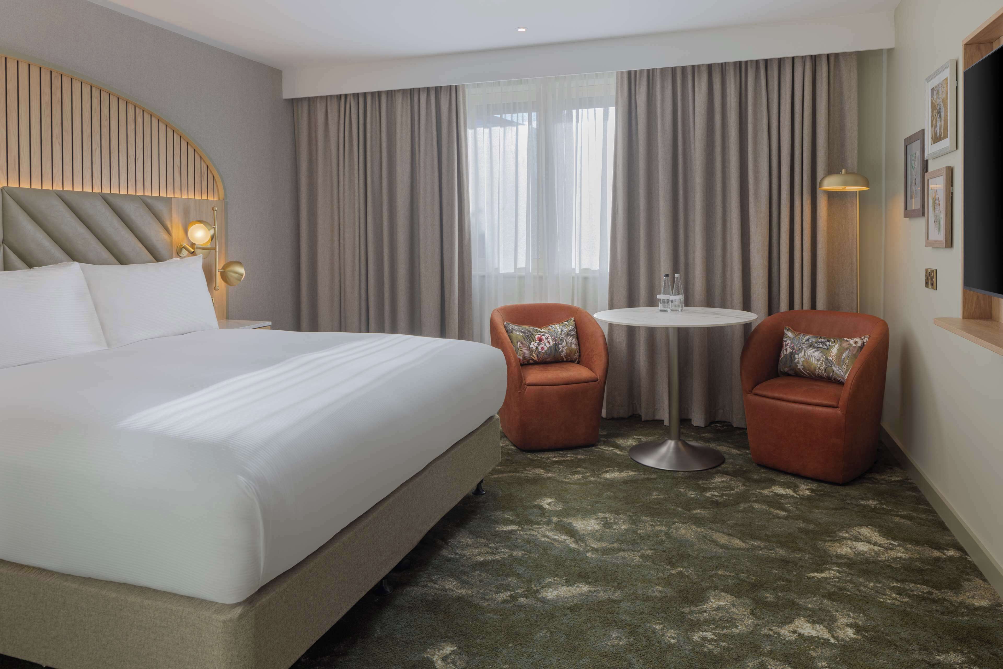 A hotel room with a large bed, two armchairs, a small round table, and a TV.