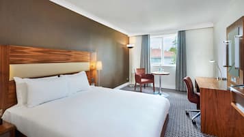 Habitació d'hotel amb un llit gran, una taula, una cadira, una làmpada i una finestra amb cortines.