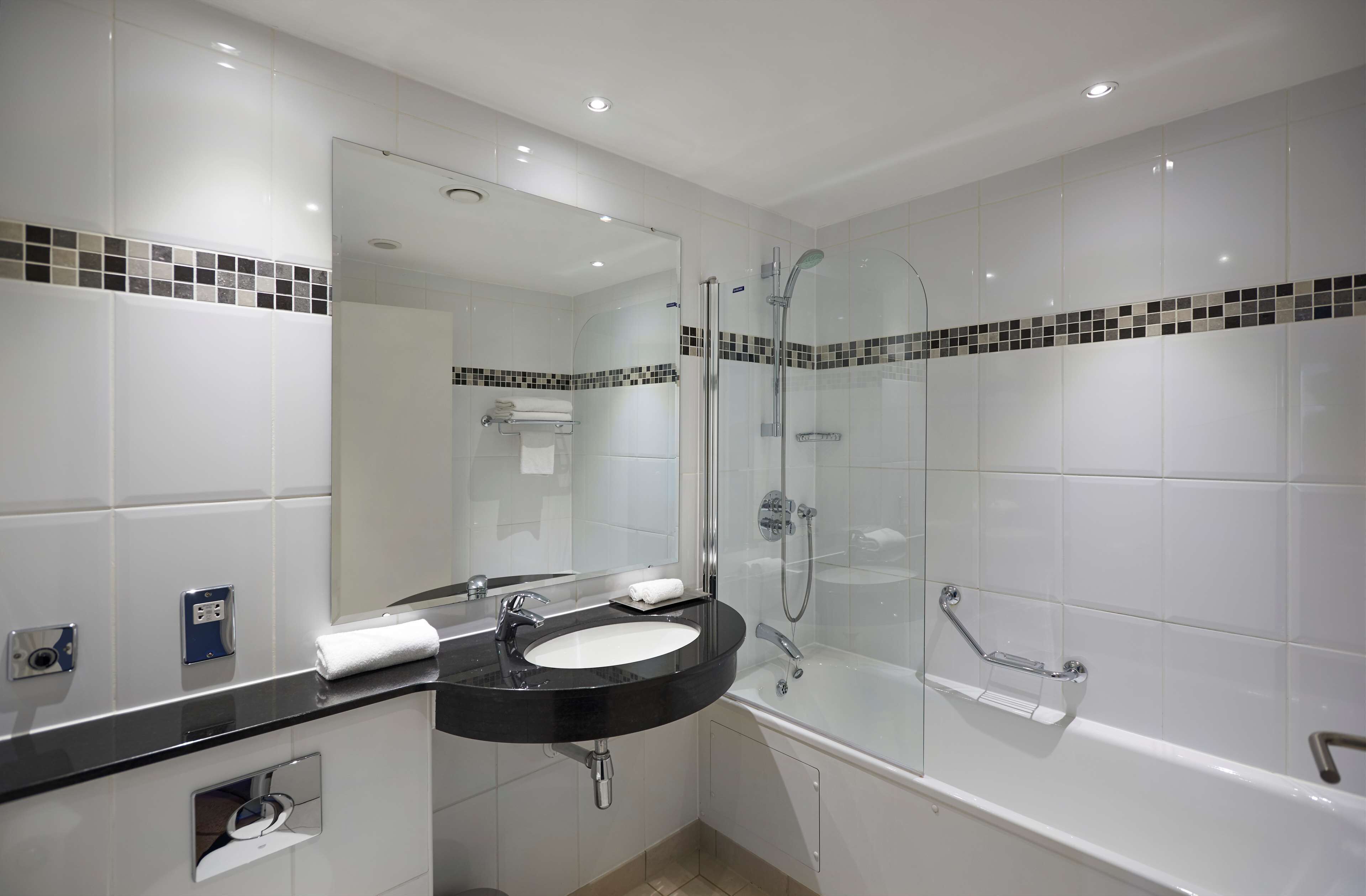 A modern bathroom with a black sink, white tiles, a glass-enclosed shower, and a mirror above the sink.
